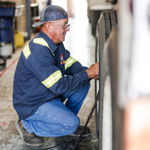 Passenger Car Motor Oils Experienced technician performing vehicle maintenance in a service bay, checking a commercial truck tire while wearing safety gear. Midtex Oil supplies premium API SN motor oil and ILSAC GF-6A motor oil formulations designed to provide engine protection, fuel efficiency, wear resistance, and reliable performance for gasoline-powered vehicles and commercial fleets.